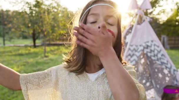 Tvář malé dívky oblečené jako Indián. Dívka s tmavými vlasy a malovanou tváří. Peří na hlavě. — Stock video