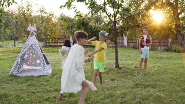 Cinco niños en el jardín jugando a los ciegos. Niños en las imágenes de los indios. Un chico está vendado. Atrapa a otros niños. — Vídeos de Stock