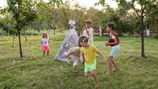 Fünf Kinder im Garten spielen mit verbundenen Augen. Kinder in den Bildern der Indianer. Mädchen mit verbundenen Augen. — Stockvideo