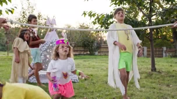 Kinderurlaub. Fünf als Indianer verkleidete Kinder hatten Spaß. Zwei Mädchen und drei Jungen spielen Spiele im Garten. — Stockvideo