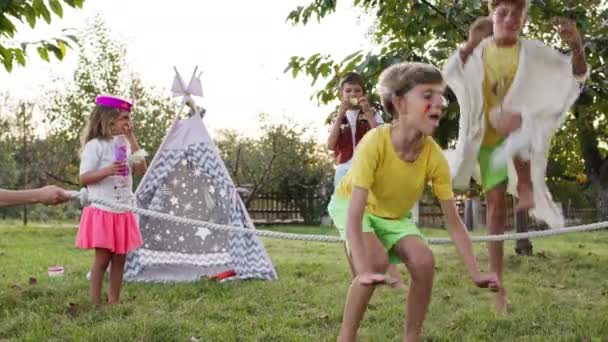 子供の休日。5人の子供が楽しみを持っているインディアンとして服を着た。2人の女の子と3人の男の子が庭でゲームをプレイ. — ストック動画