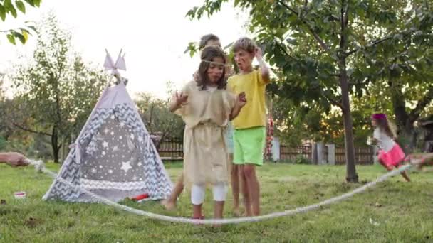 Kinderfeestdagen. Vijf kinderen gekleed als indianen hebben plezier. Twee meisjes en drie jongens spelen spelletjes in de tuin. — Stockvideo