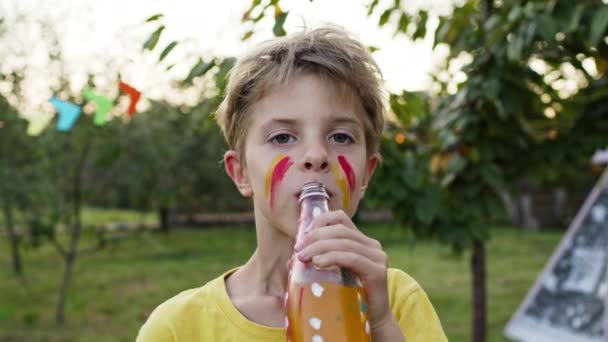 Kinderfeestdagen. Jongensdrankjes uit een fles sap. Hij heeft een beschilderd gezicht. Hij lijkt op een indiaan.. — Stockvideo