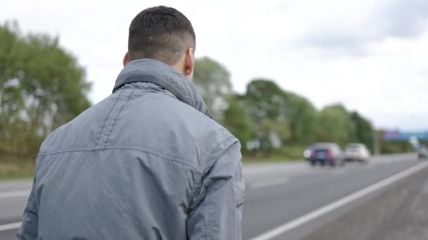 Back Of Young Man Walking Down The Road Driving Cars (em inglês). escuro cabelos cara no cinza jaqueta. — Vídeo de Stock