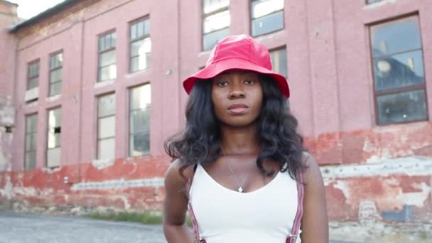 Retrato da jovem garota negra na rua. Ela fica com uma expressão séria no rosto. Menina de chapéu com cabelo comprido. — Vídeo de Stock