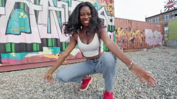 Junge schwarze Mädchen auf der Straße hocken auf dem Boden. Sie tanzt auf der Straße. Mädchen macht Luftküsse und lächelt. — Stockvideo