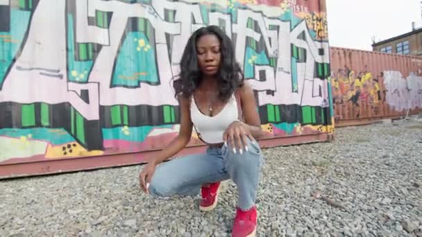 Rapariga negra na rua agachamentos no chão. Ela dança na rua. Atrás dela nas paredes do Graffiti. — Vídeo de Stock