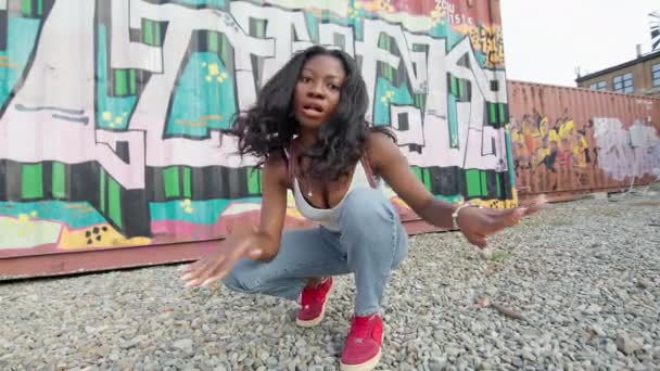 Rapariga negra na rua agachamentos no chão. Ela dança na rua. Atrás dela nas paredes do Graffiti. — Vídeo de Stock
