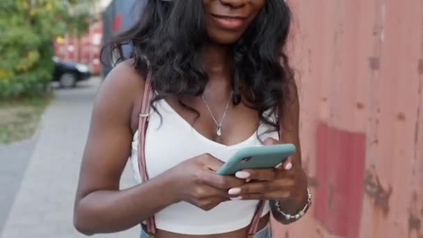 Krásná černošky dívka kráčí po ulici s mobilním telefonem ve svých rukou. Podívá se na obrazovku telefonu a usměje se. Dívka začíná tancovat. — Stock video