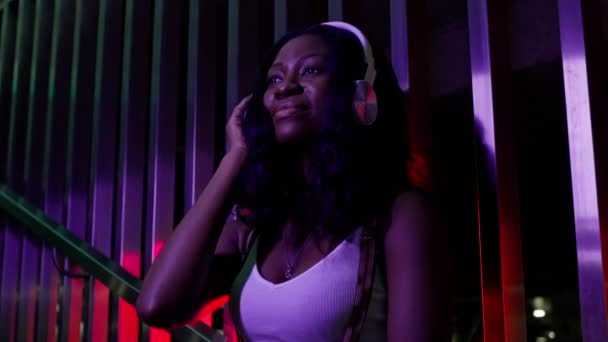 Glimlachend zwart meisje dat naar muziek luistert. Op haar koptelefoon. Ze glimlacht en beweegt naar het ritme van de muziek. — Stockvideo