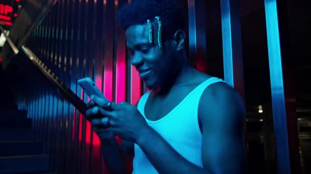 Ένας νεαρός μαύρος με τηλέφωνο στα χέρια του. Στέκεται στις σκάλες κοντά στο υπόγειο πάρκινγκ και σκιάχτρα. Ανοιχτό μπλε και ροζ χρώματα. — Αρχείο Βίντεο