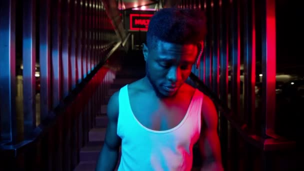 젊은 흑인이 손에 전화기를 들고 있다. 그는 지하 주차장 근처에 있는 계단으로 내려갔다. 밝은 파랑과 분홍 빛의 어두운 색깔. — 비디오