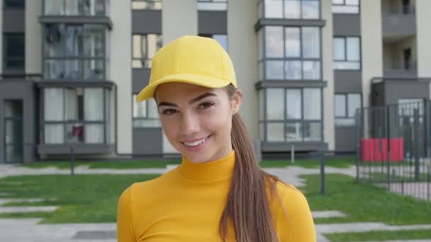 Młoda dziewczyna doręczycielka na ulicy. Ładna brunetka w żółtej czapce i swetrze. — Wideo stockowe