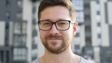 Gözlüklü genç bir adamın yüzü. Sokakta durur ve gülümser..