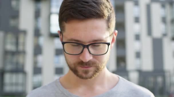 Porträt eines jungen Mannes mit Bart und Brille. Hinter ihm mehrstöckiges Gebäude. — Stockvideo