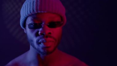 Siyah adam karanlık odada güneş gözlüklü ve şapkalı. Adam kadehini kaldırıp göz kırpıyor..