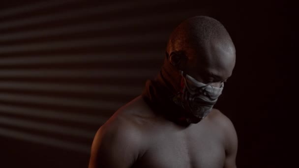Чорний хлопець у темній кімнаті з хустиною на роті. — стокове відео