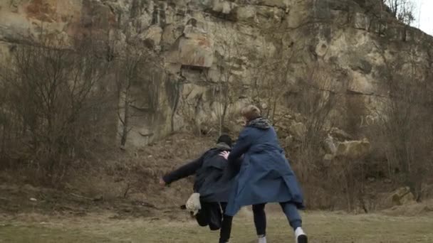 Deux jeunes gars qui courent vers l'avant. Les gars en imperméable sur fond rocheux. Vue de l'arrière. — Video