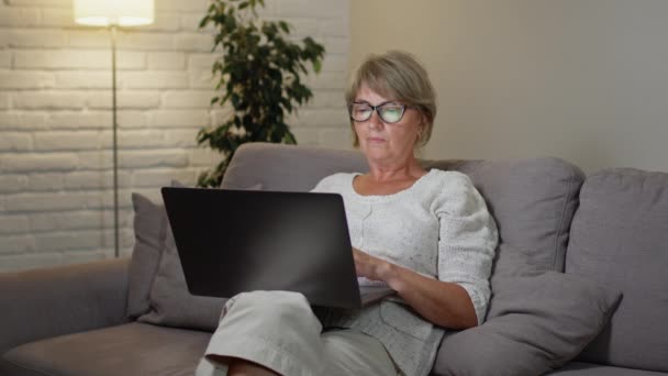 Жінка використовує ноутбук. Вона сидить на дивані і масажує спину. Жінка втомилася . — стокове відео