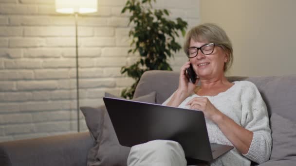 Pretty Middle Aged Woman Sitting In Front Of Laptop. Someone Is Calling And She Is Having Fun Talking On Her Cell Phone. — Stock Video