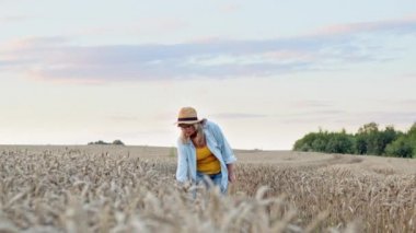Güzel Sarışın, Buğday Kulağı 'na eliyle dokunuyor. Şapkalı Güzel Kadın Buğday Tarlasında Yolda Yürüyor.