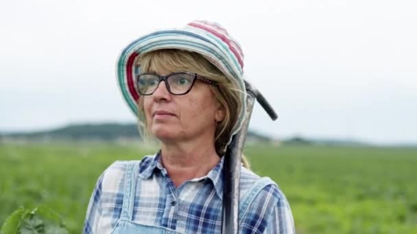 甜菜田里农民妇女的脸。和Shovel一起散步的女人眼镜和帽子中的中年金发美女. — 图库视频影像