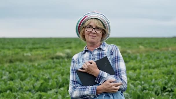 Женщина-фермер, стоящая посреди свекловичного поля с табличкой в руках. Женщина в комбинезоне и шляпе. — стоковое видео