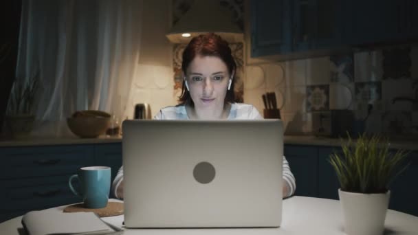 Femme dans la cuisine avec ordinateur portable. Quelque chose la surprend et elle sourit. — Video