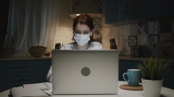 带笔记本电脑厨房里的小女孩。医疗面具中的女性在记事本上做笔记. — 图库视频影像