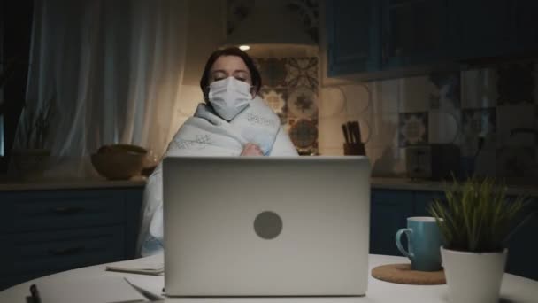 Ung flicka i köket med laptop. Ung kvinna arbetar på distans hemma på grund av en pandemi. Kvinna i medicinsk mask. — Stockvideo