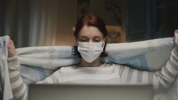 Jong meisje in de keuken met laptop. Jonge vrouw die op afstand thuis werkt vanwege een pandemie. Vrouw in het medische masker. — Stockvideo