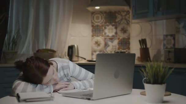 Kvinnan i köket med laptop. Trött ung kvinna sover på skrivbordet nära laptop. — Stockvideo