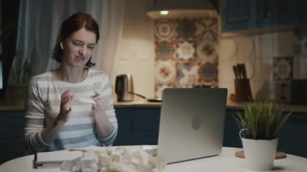 Mujer en la cocina con ordenador portátil. Ella arranca las hojas de su cuaderno y las tira. — Vídeos de Stock