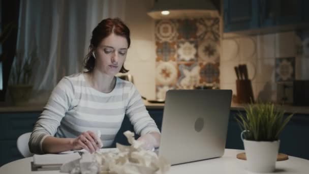 Mujer en la cocina con ordenador portátil. Ella arranca las hojas de su cuaderno y las tira. — Vídeo de stock