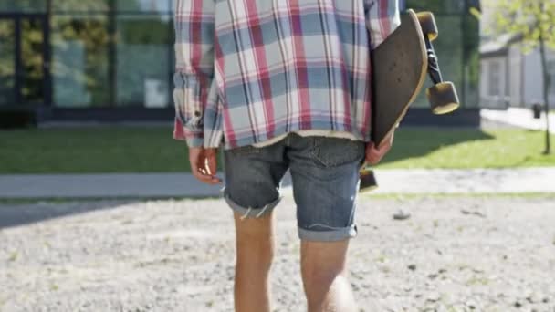 Il tizio cammina per strada con lo skateboard. Viso invisibile. ragazzo in pantaloncini e giacca. — Video Stock