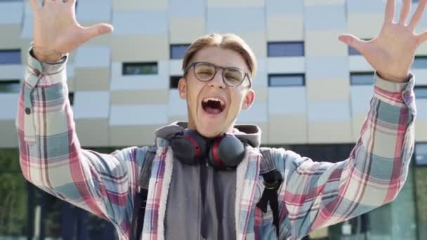 Porträt eines jungen Mannes auf der Straße. Schöner Kerl mit Brille und Kopfhörer um den Hals. Guy lächelt und sagt Wow. — Stockvideo