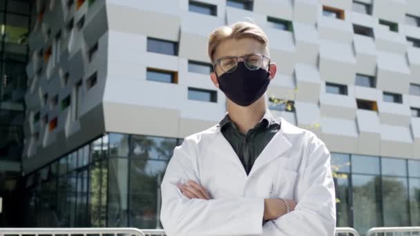 Guy In White Coat Stands On The Background Of Tall Building. Young Guy With Glasses. He Is Scientist Or Physician. — Stock Video