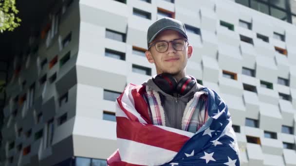 Retrato de um jovem na rua. Ele tem a bandeira dos EUA nas costas. — Vídeo de Stock