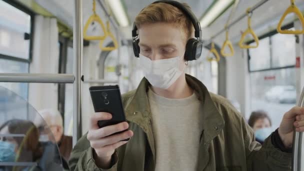 Giovane ragazzo sale in autobus con maschera medica sul viso. Proteggere la salute in un'epidemia. Guy utilizza il telefono cellulare — Video Stock