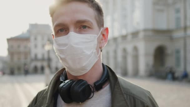 Fiatal fickó orvosi maszkkal az arcán. Egészségvédelem egy járványban. Egy fickó áll az üres utcán.. — Stock videók