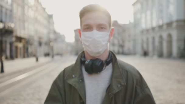 Ung kille med medicinsk mask på ansiktet. Skydda hälsan i en epidemi. Guy stående på tom gata. — Stockvideo