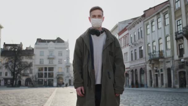 Jeune homme avec un masque médical sur le visage. Protéger la santé en cas d'épidémie. Guy debout sur la rue vide. — Video