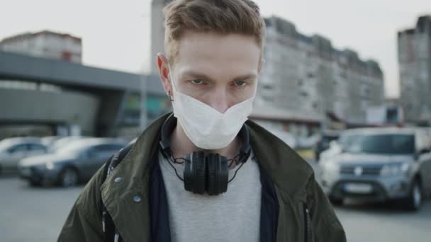 Fiatal fickó orvosi maszkkal az arcán. Egészségvédelem egy járványban. Egy fickó áll az utcán.. — Stock videók