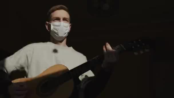 Хлопець у медичній масці. Сумний погляд. Молодий хлопець грає гітару . — стокове відео