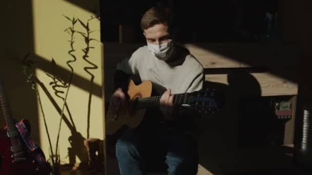 Maschera Medica. Che sguardo triste. Giovane ragazzo che suona la chitarra. Ragazzo nel suo appartamento. — Video Stock