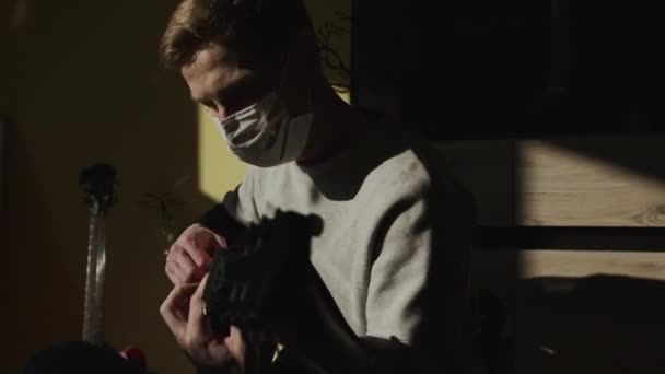 医療マスクの男。悲しい顔だ。若い男がギターを弾く。彼のアパートで男. — ストック動画