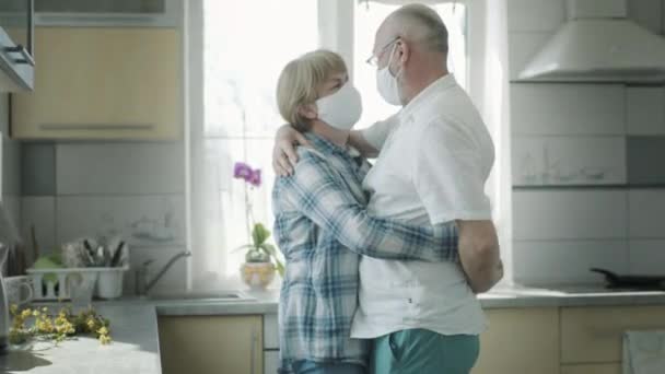 Мужчина и женщина в медицинских масках танцуют на кухне. — стоковое видео