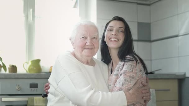 Alte Frau umarmt ihre junge Enkelin. Frau in der Küche. — Stockvideo