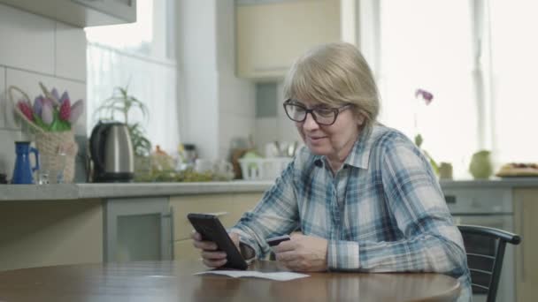 Mulher sentada na cozinha na mesa com celular nas mãos. — Vídeo de Stock