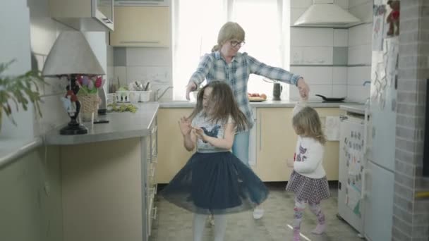 Grand-mère danse dans la cuisine avec deux petites-filles. — Video